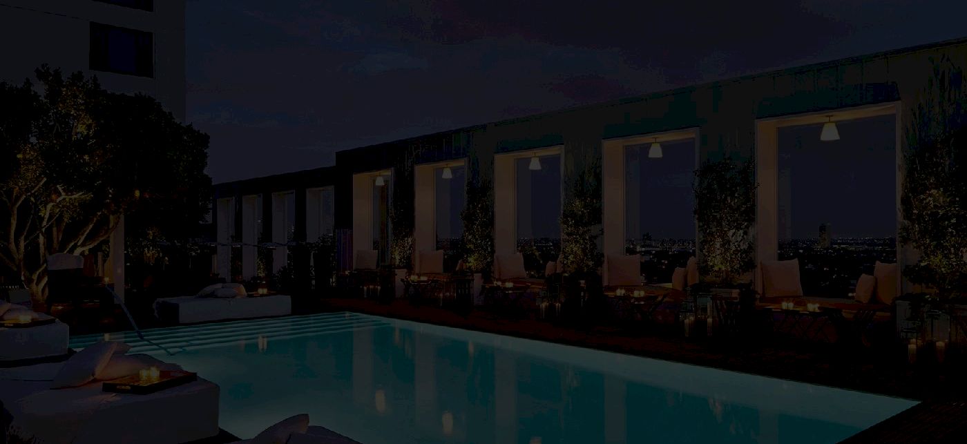 A nighttime pool area with lounge chairs along a rectangular pool, modern buildings in the background, dim lighting and reflective water, ending here.