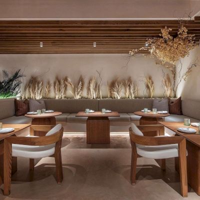 A stylish, modern dining area with wooden tables, white chairs, a long cushioned back bench, and warm decorative lighting.