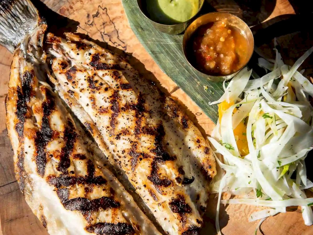 Grilled fish steak on a wooden board, with lime wedges, sliced onions, and three small sauces on the side. Done.
