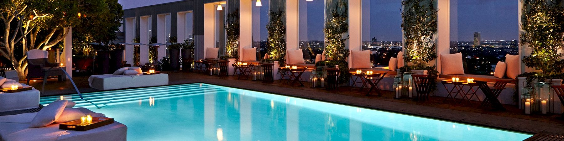 A luxurious rooftop pool at dusk with lounge chairs, warm lighting, and glass-walled cabanas overlooking a city skyline, serene and upscale.