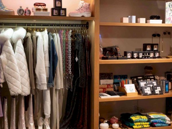 A boutique clothing rack with hanging coats and dresses on the left, and shelves with small accessories and folded items on the right.