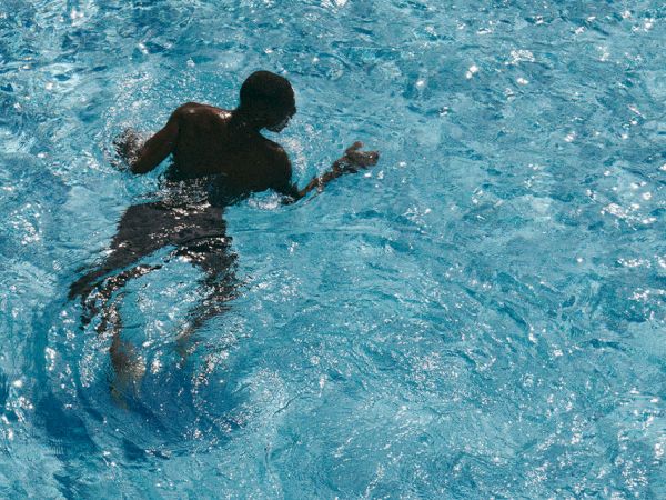 A person is swimming or treading water in a bright blue pool, paddling with arms as they move through the water.