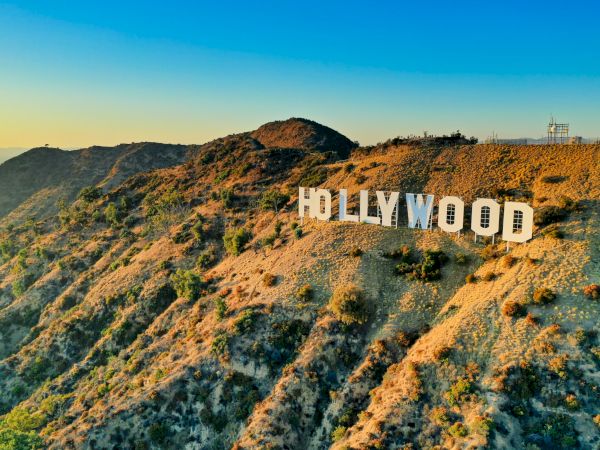 The Hollywood sign sits on a rugged hillside under a blue-to-orange sunset sky.